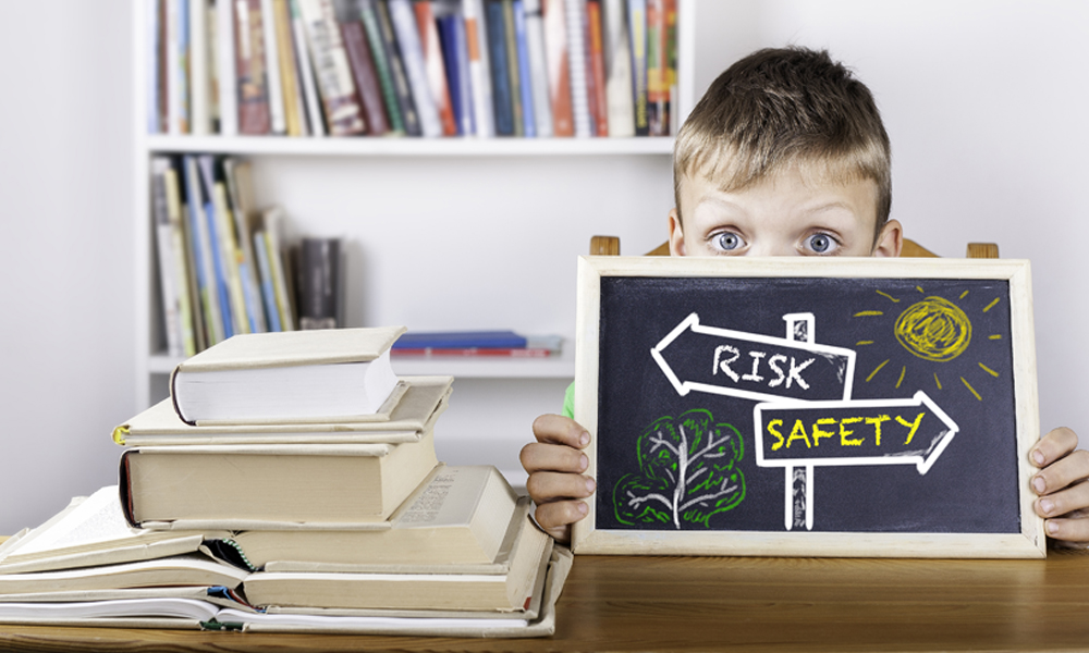 young boy holding up a black board with the sign risk and safety