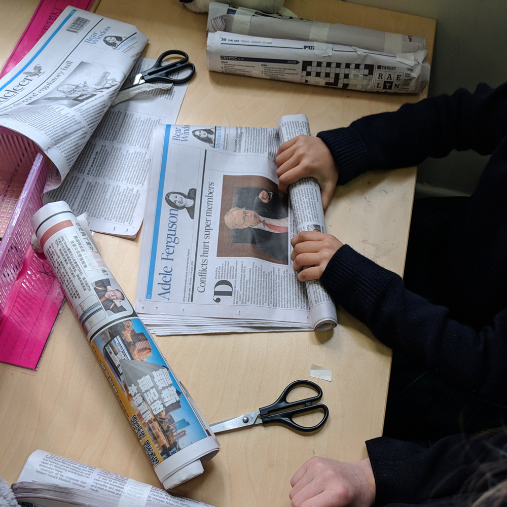 Makerspace newspaper challenge showing kid rolling newspaper on desk