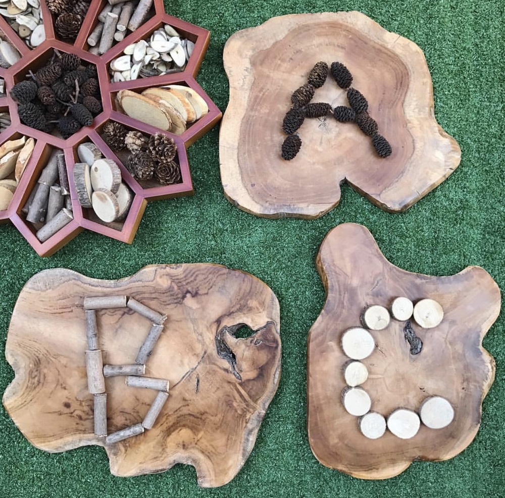 Natural resources such as pinecones, twigs and branch cuts are used to create and form the letters of the alphabet on natural wooden slices
