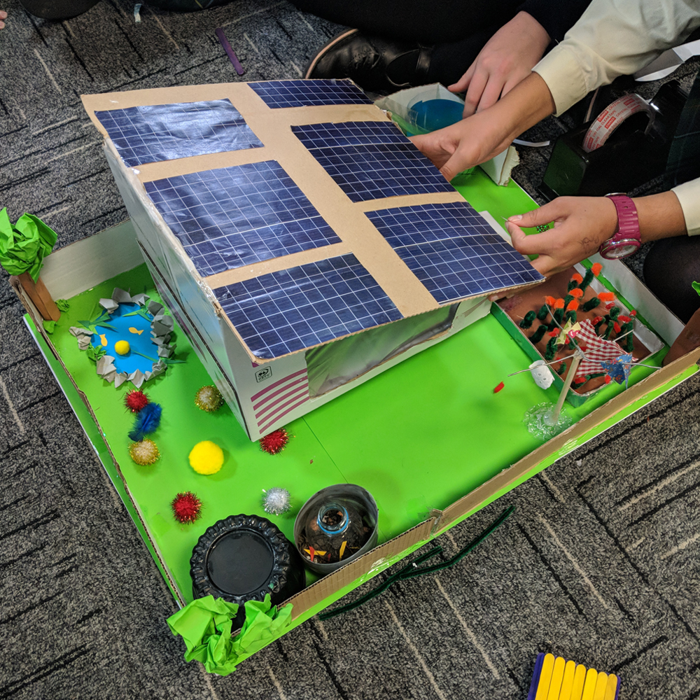 Child creating Sam Labs sustainability house with solar panels and garden made out of card