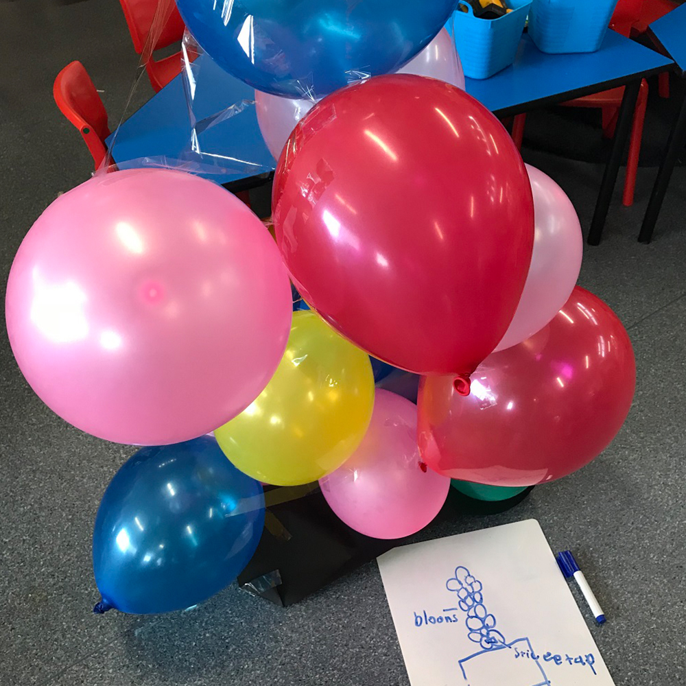 Balloons stacked in a tower with a drawing on paper of intended outcome