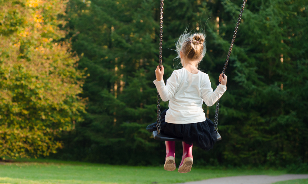 Girl playing on swing outside facing grass and trees