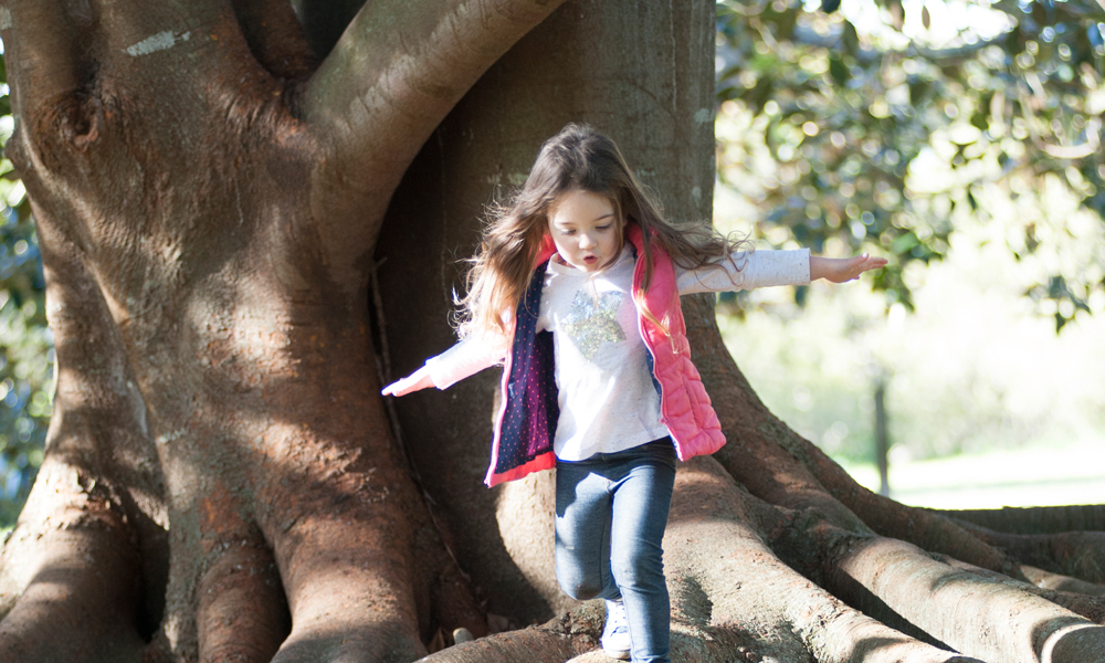 Young girl exploring whilst walking over tree roots
