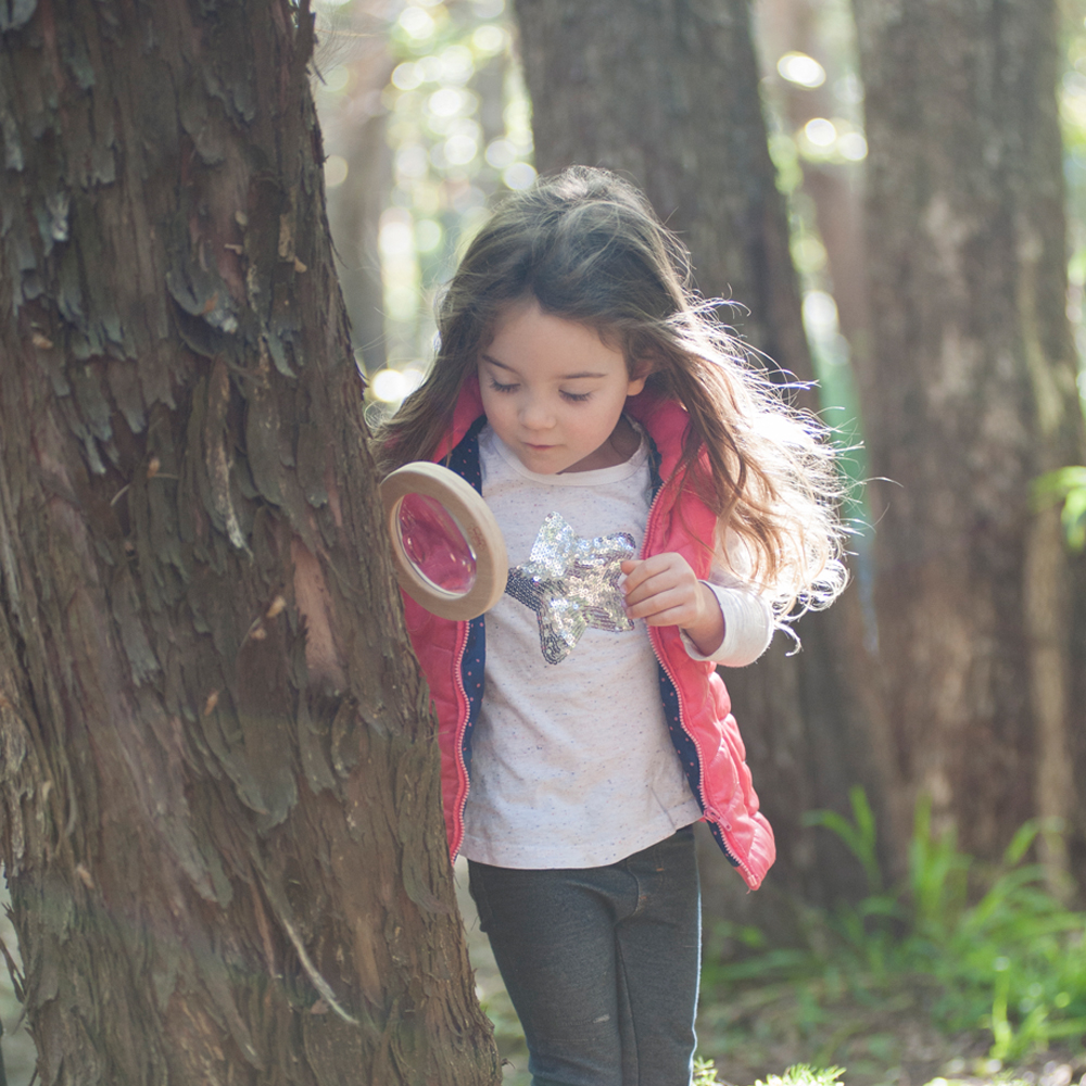 Young girl exploring the outdoors with magnifier glass