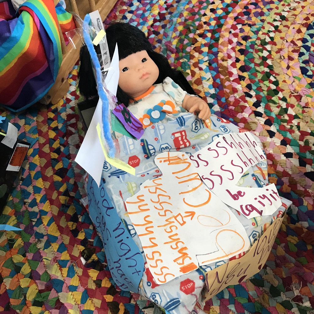 Doll in bed personalised with messages and drawings on blanket made of white paper