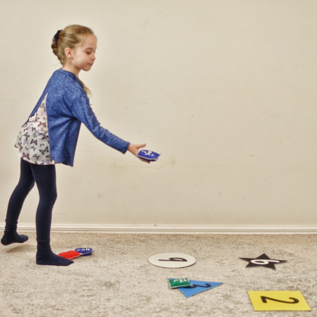 Staying Active at Home. Girl exploring numeracy activity throwing numbered beanbags on numbered squares