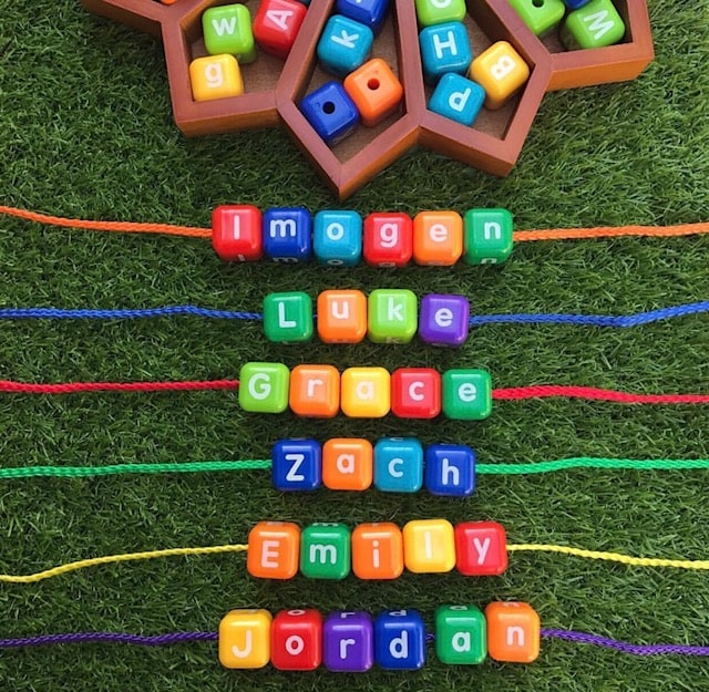 Threading letter beads spelling out childrens names on grass background