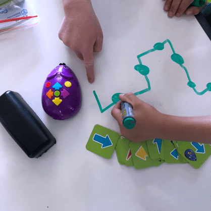 Robot mouse coding cards child's hands drawing path using whiteboard marker