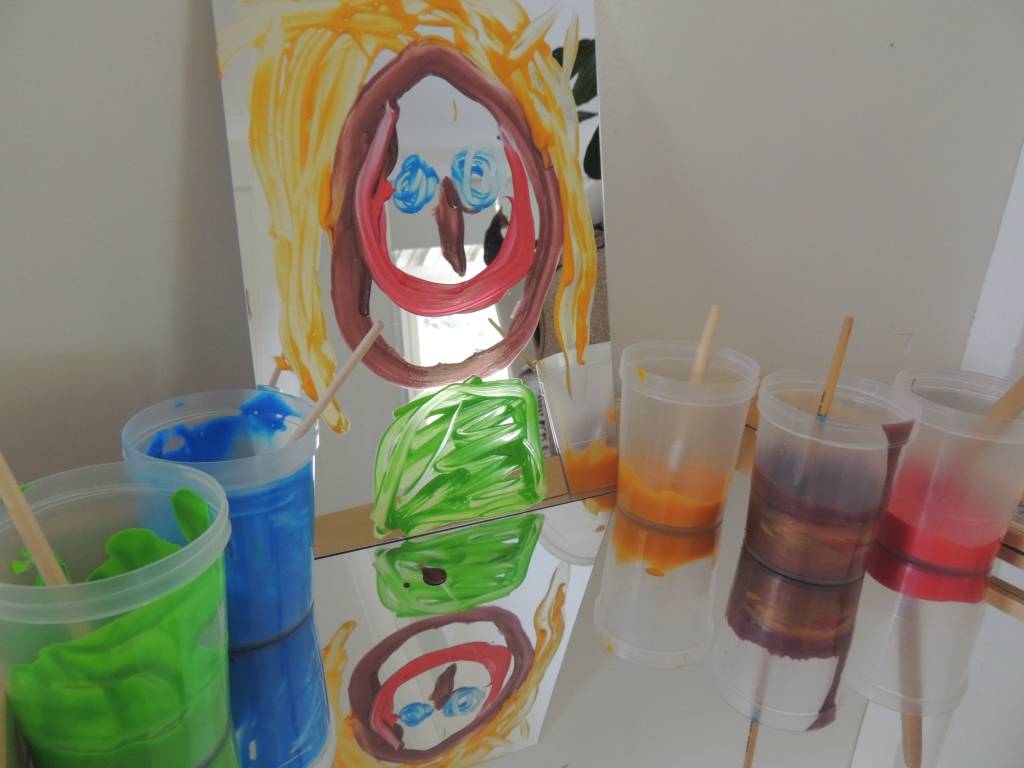 Mirrors and Reflections portrait activity featuring childs painting on a mirror and paint pots