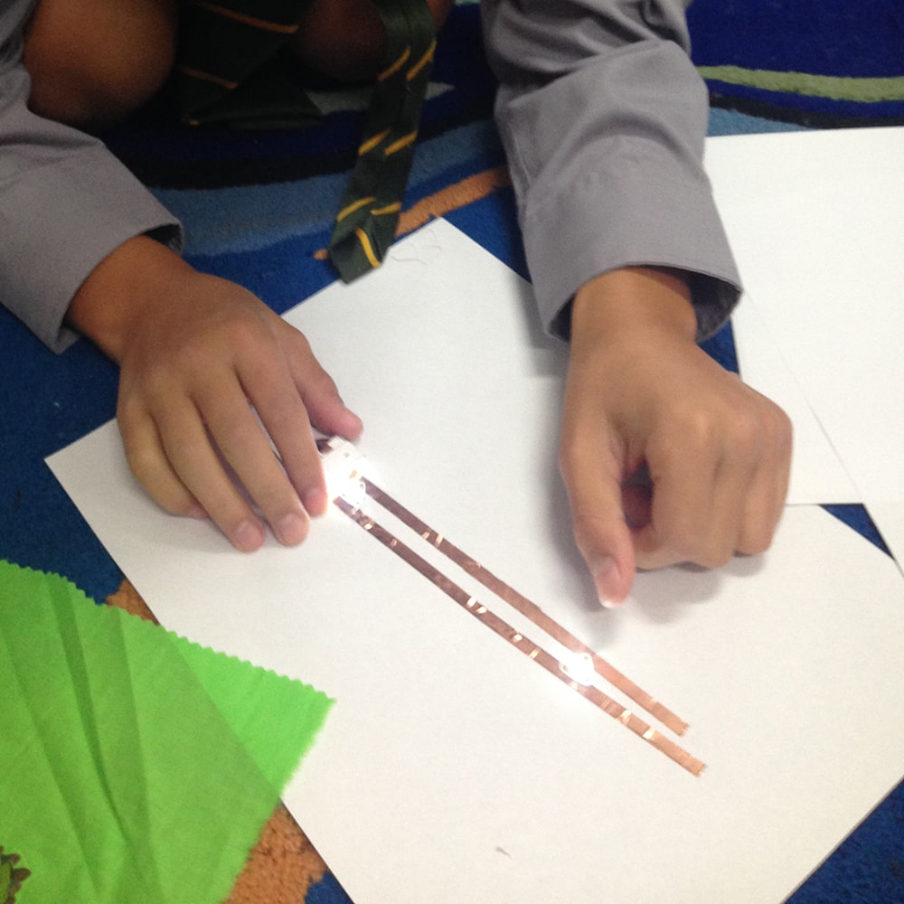 Embroidery Character Circuit building featuring child's hands, paper and copper circuit wire