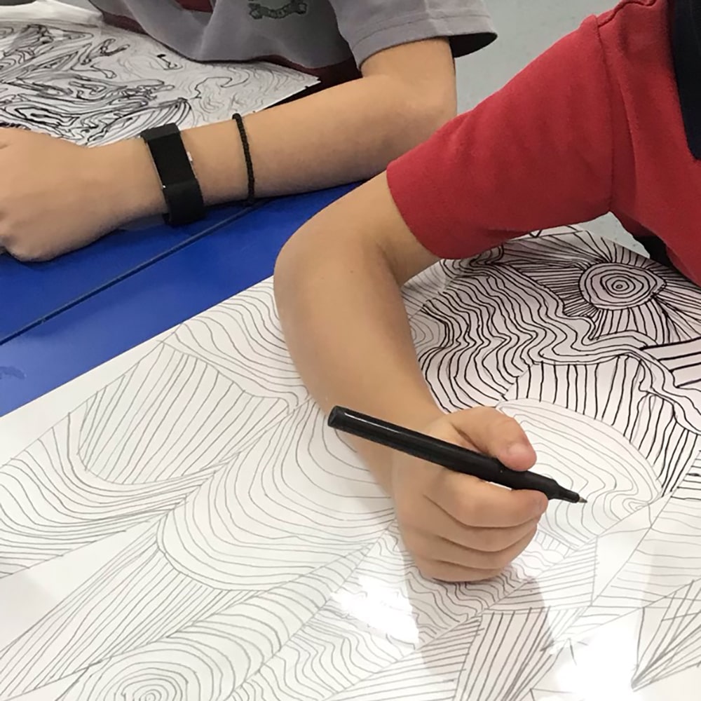 Student working on Map Overlay art Example, featuring student's arms, pen, paper & desk