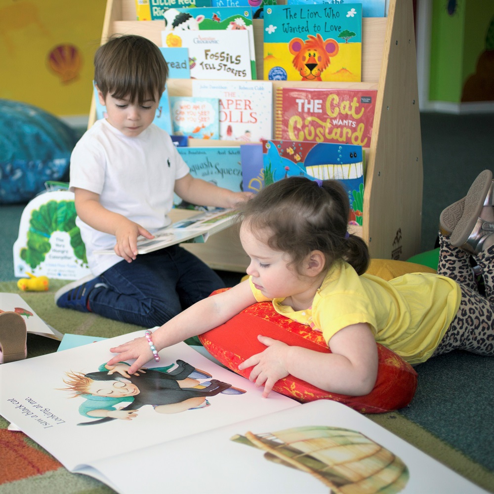 Young girl and boy reading large storybooks in earlychildhood centre classroom